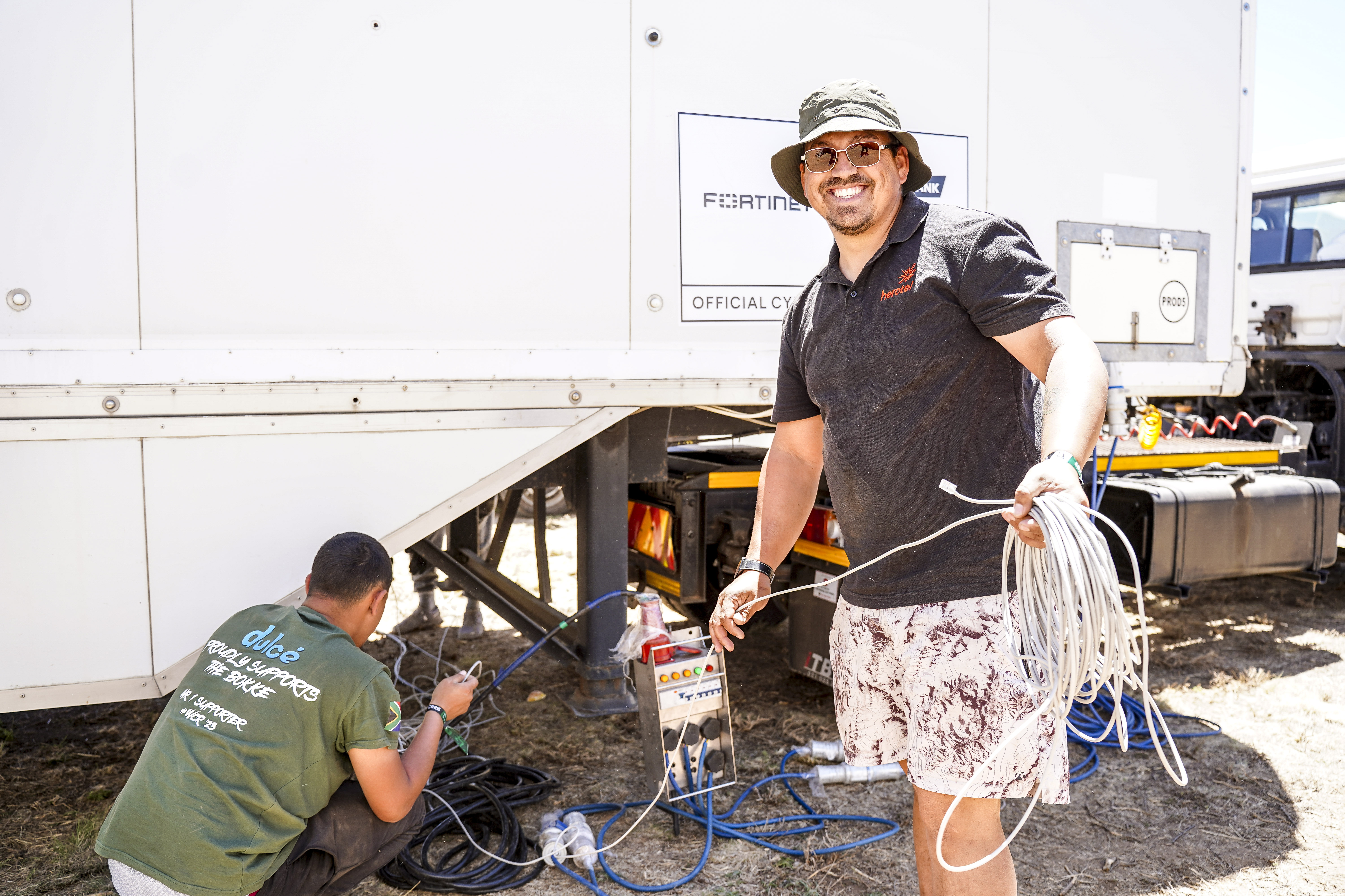 A person wearing a Herotel shirt holds network cabling beside an event communications vehicle.
